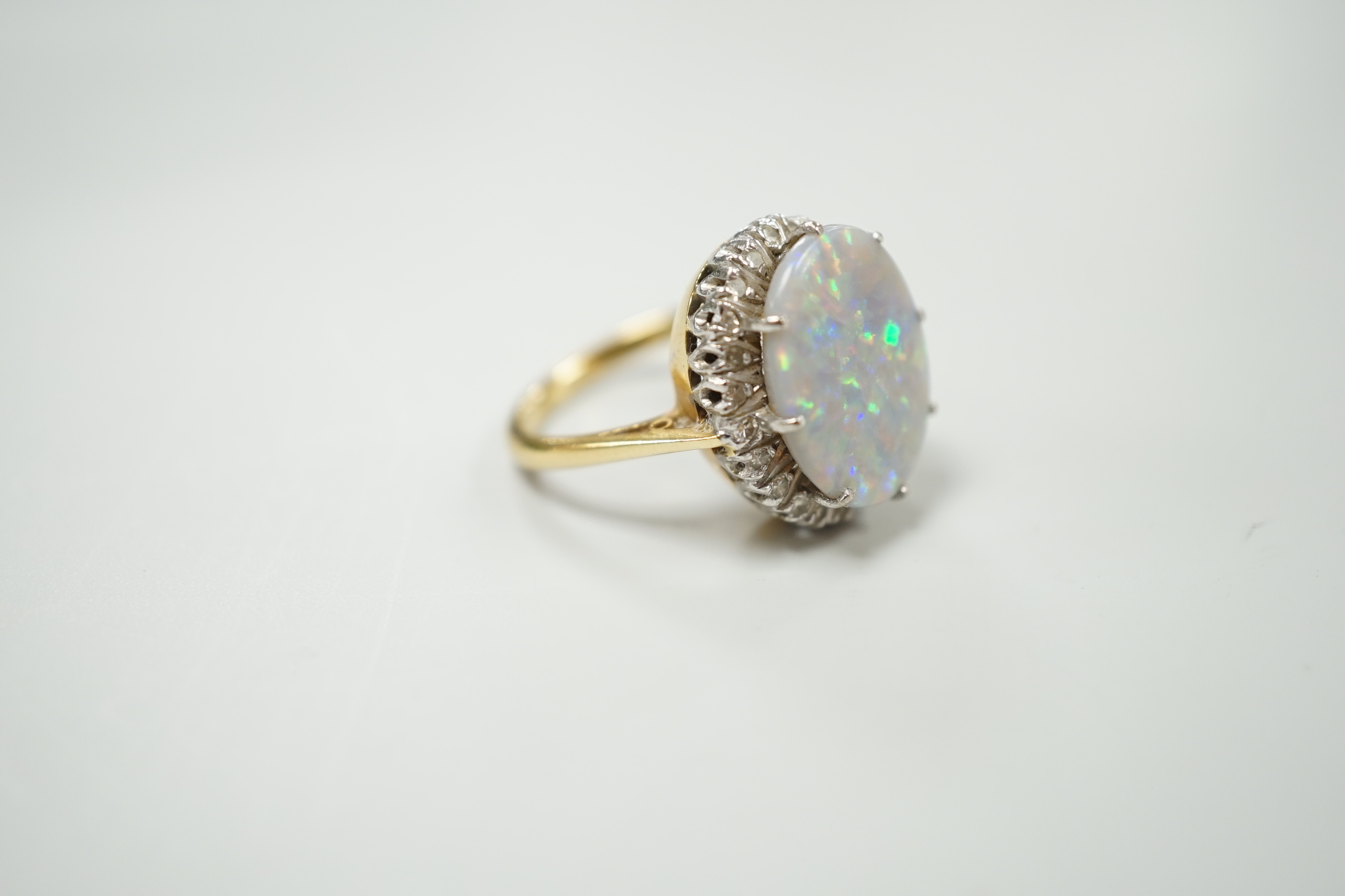 An 18ct, white opal and diamond chip set oval cluster ring, size L, gross weight 8.1 grams.